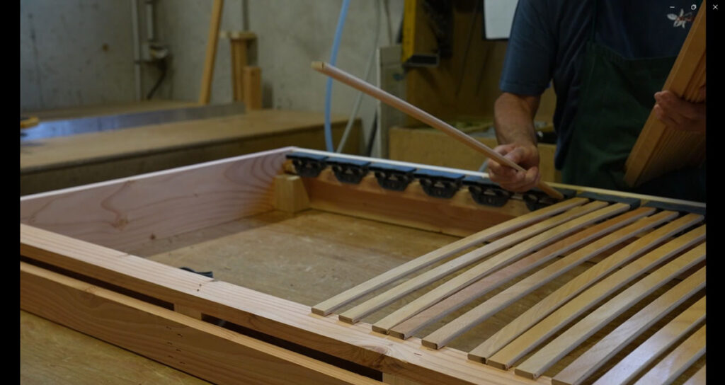 Pose des lattes en bois sur un sommier tapissier fabriqué en France dans l'atelier OX Literie