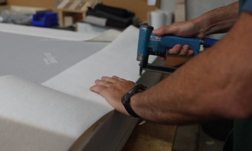Découpe et pose de la toile de recouvrement sur un sommier tapissier habillé dans l'atelier OX Literie